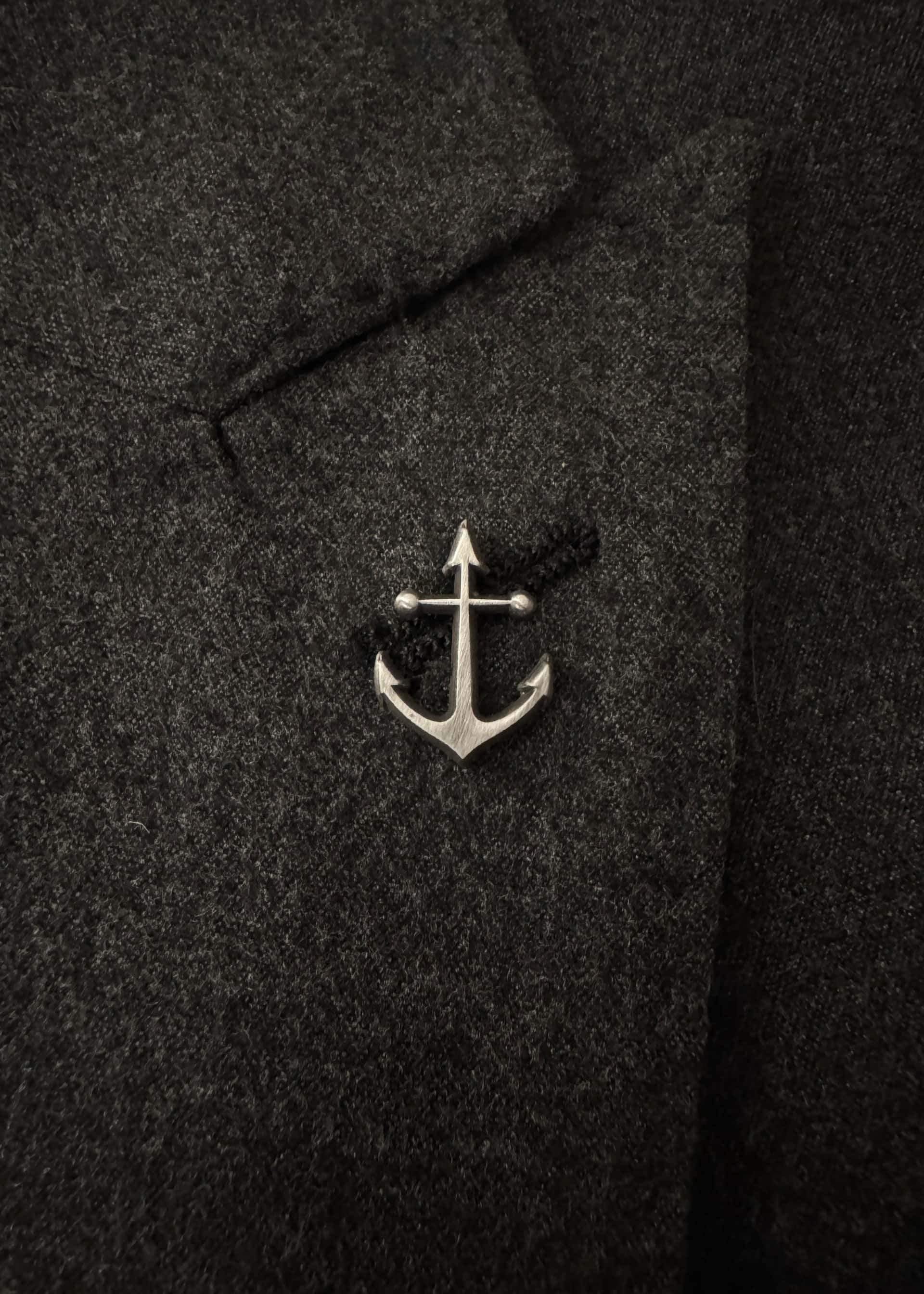 The anchor pin in antique nickel, worn on a dark flannel lapel
