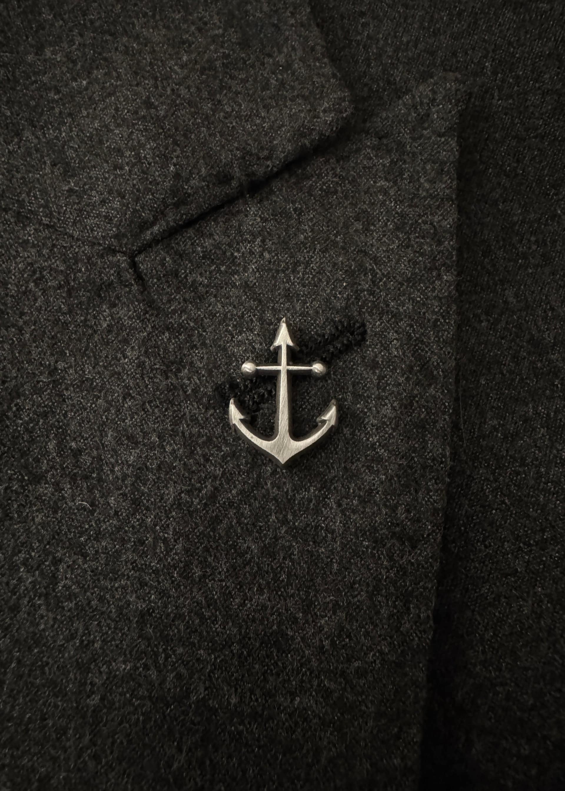 The anchor pin in antique nickel, worn on a dark flannel lapel