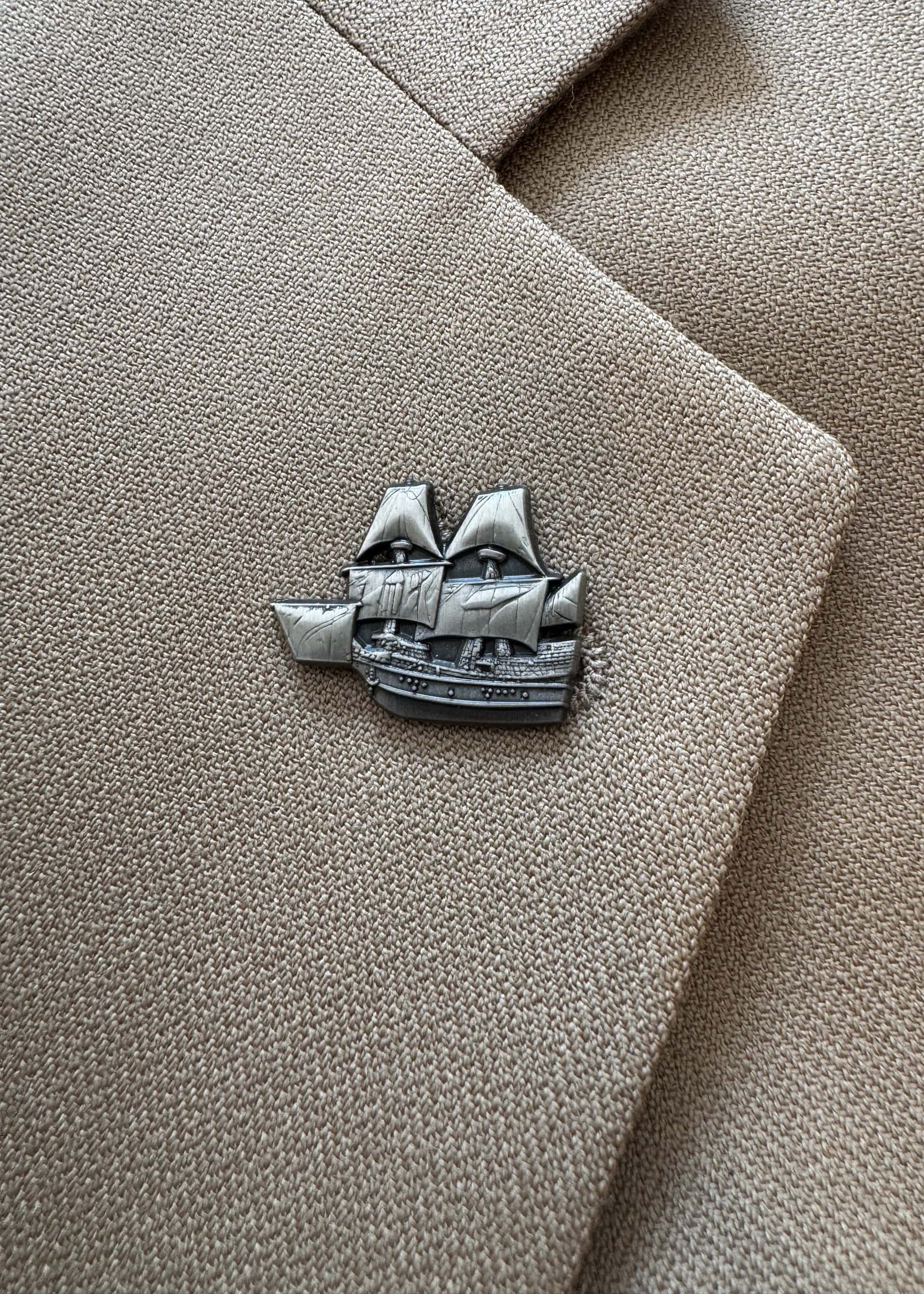 The Mayflower pin in antique nickel, worn on a tan suit lapel