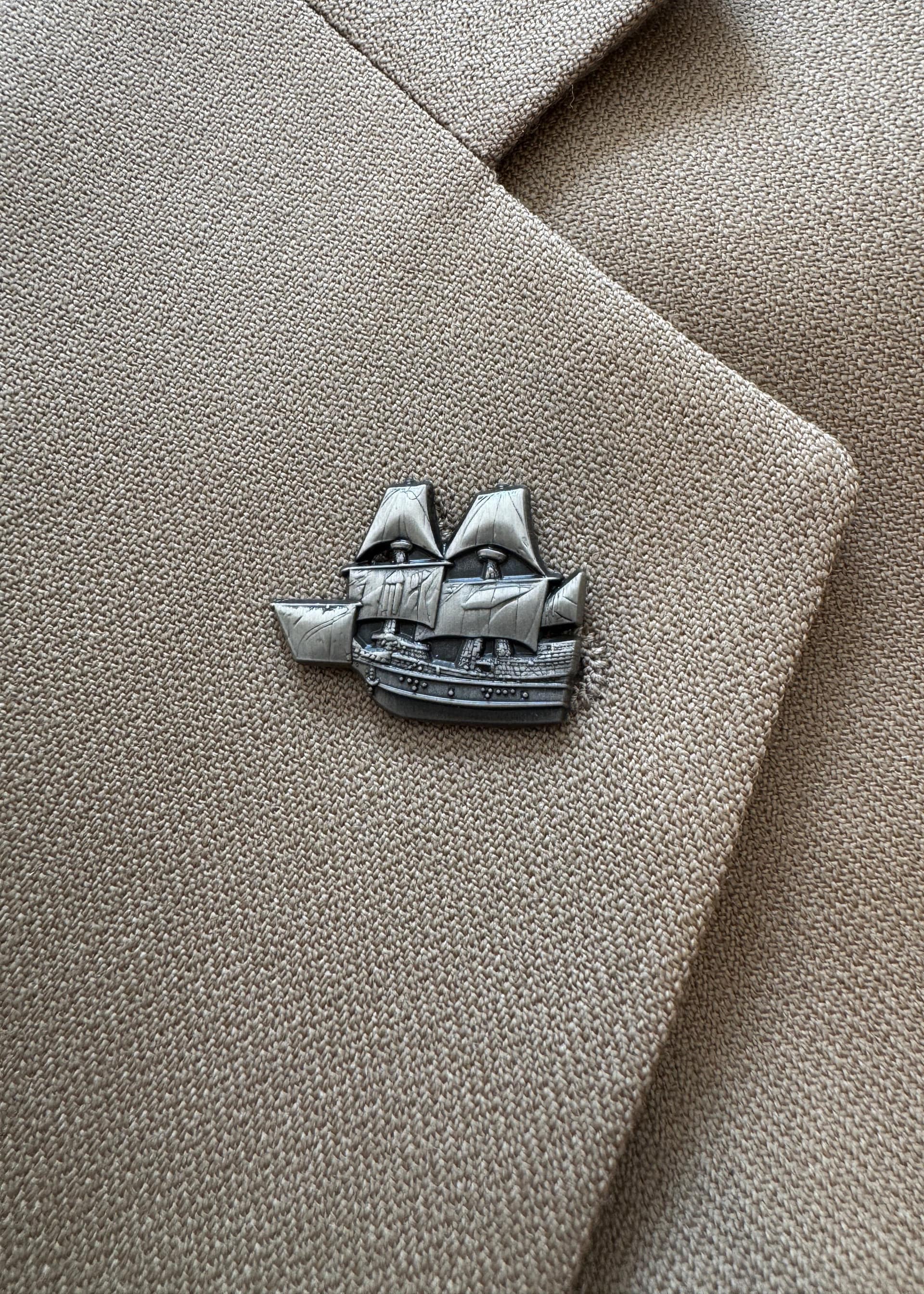The Mayflower pin in antique nickel, worn on a tan suit lapel