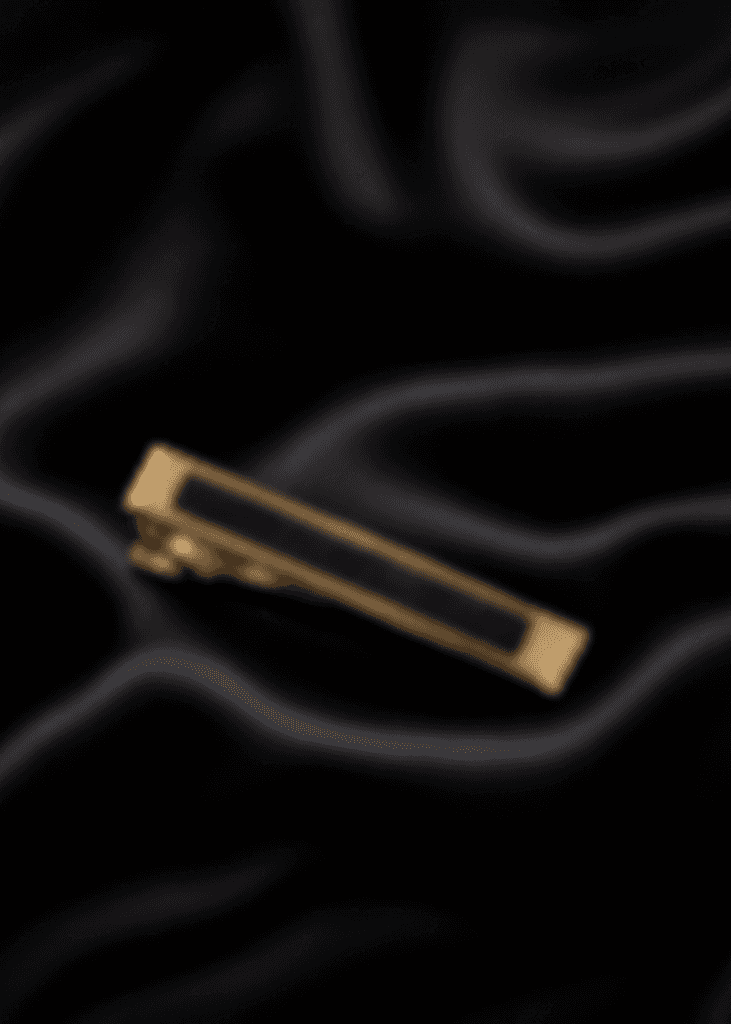 The Minuteman tie bar, gold-toned with a black inlay, laid on black satin